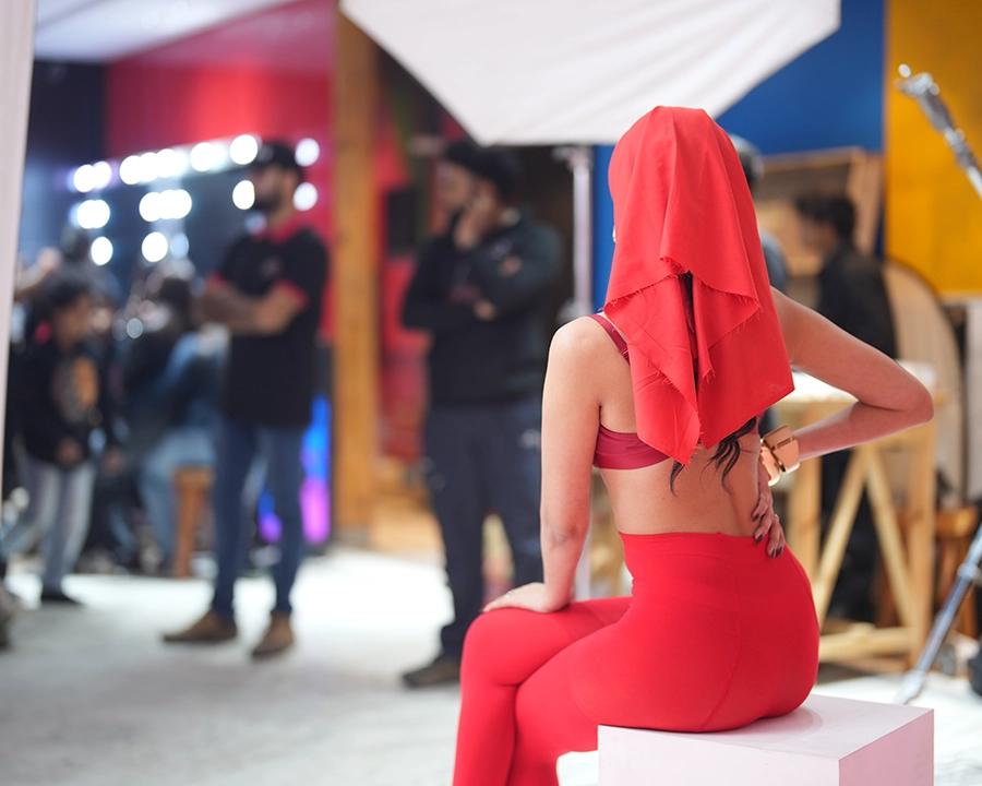 Model in a red fashion look seated on a live studio set during a guided shoot