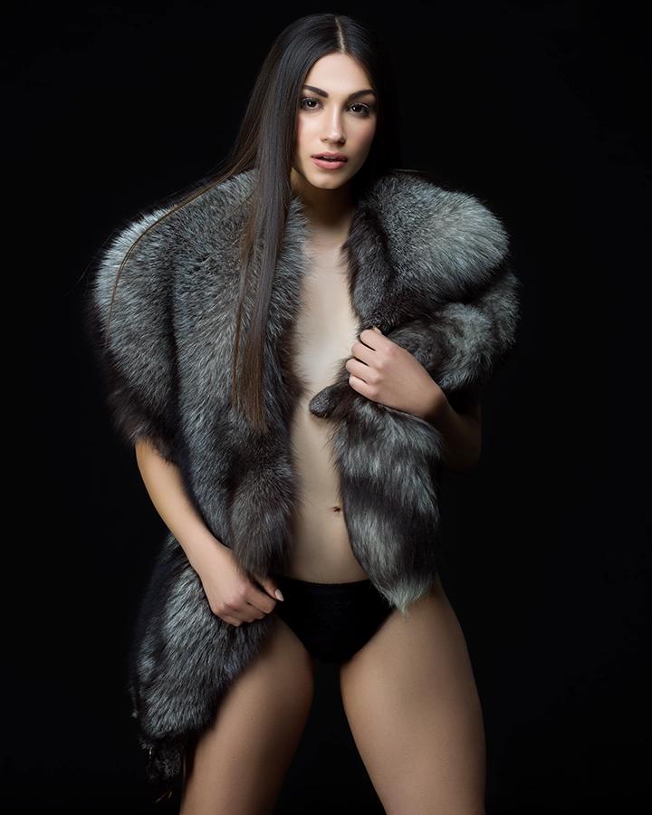 Studio fashion portrait of a model wearing a dramatic grey garment against black