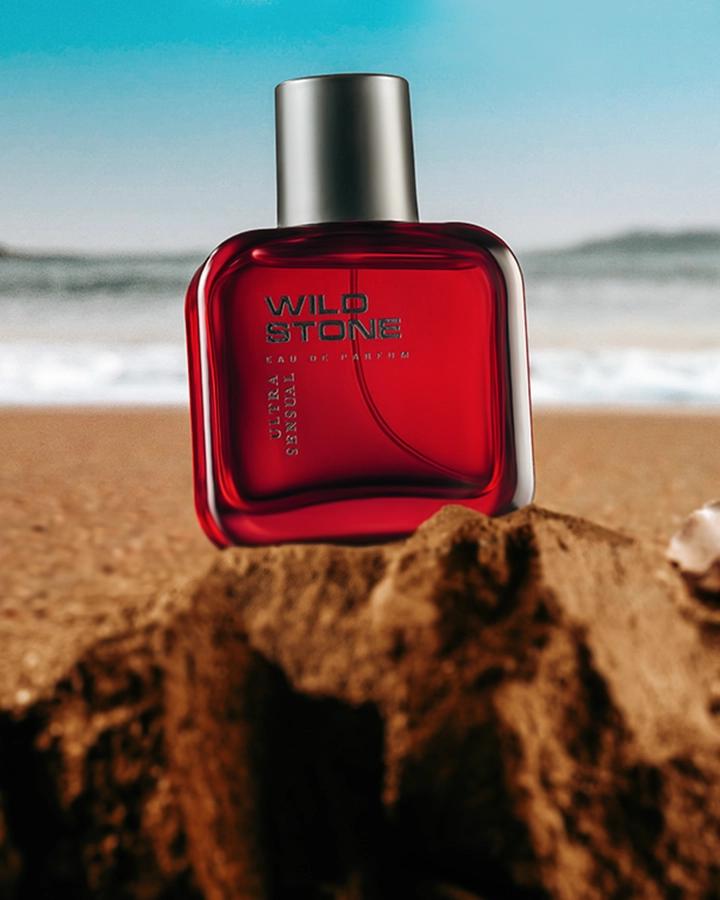 Red perfume bottle photographed in a styled beach setting for a commercial product image