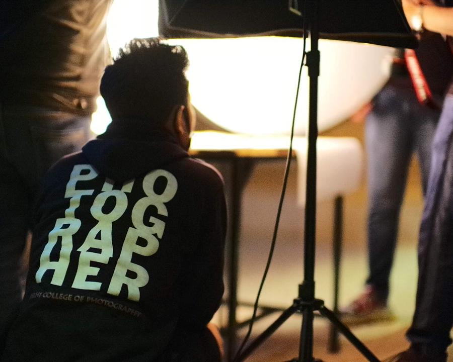 DCOP student adjusting a tabletop studio lighting setup during a guided product photography exercise