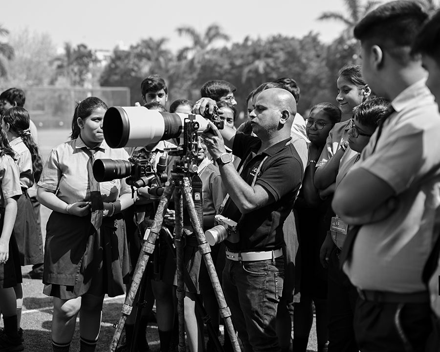 Photography instructor demonstrating a telephoto camera setup to students outdoors