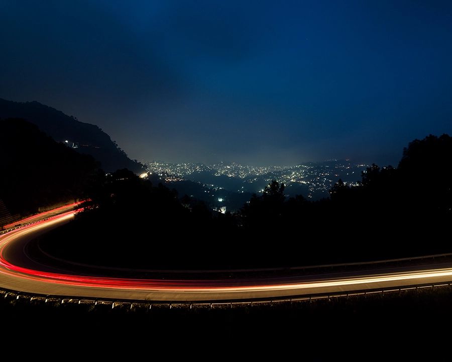 Long-exposure light trails on a mountain road overlooking a city at night